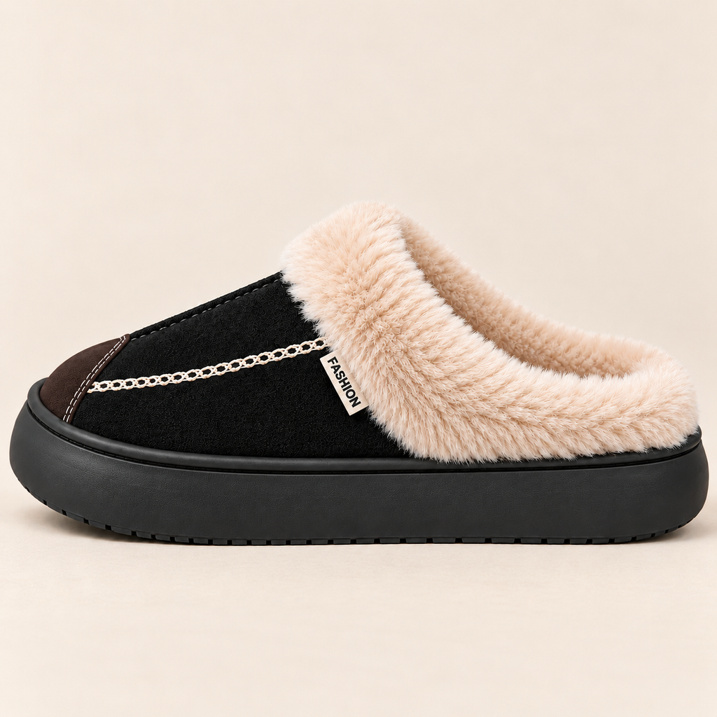 A single slip-on mule slipper shown in profile against a light beige background. The shoe has a black suede-like upper, a thick black rubber sole, a soft beige faux-fur collar, a small brown accent panel near the toe, and a decorative silver chain detail across the side.